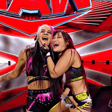 two female wrestlers are hugging and laughing in front of a large red sign that says wwe