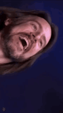 a man with long hair is laughing with his mouth open