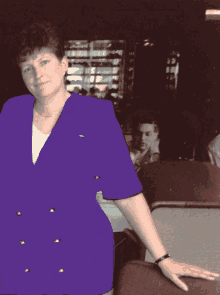 a woman in a purple jacket stands in a dark room