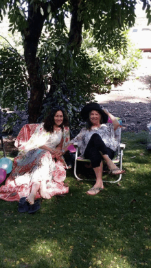 two women sit in chairs under a tree