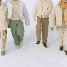 a group of people are walking in the snow wearing white jackets and green pants