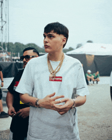 a man wearing a white supreme t-shirt with gold chains around his neck