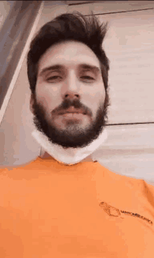 a man with a beard is wearing a face mask and an orange shirt .