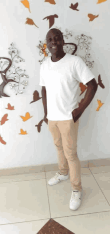 a man wearing a white shirt and khaki pants stands in front of a wall with birds on it