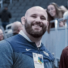 a bald man with a beard is smiling in a stadium while wearing a name tag .