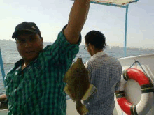 a man in a plaid shirt is holding a fish in his hand on a boat .