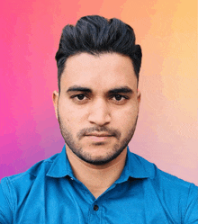 a man with a beard wearing a blue shirt looks at the camera