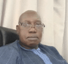 a man wearing glasses and a blue shirt is sitting in a chair and looking at the camera .