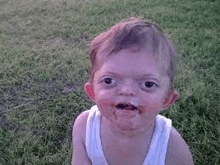 a baby with a dirty face is sitting in the grass and making a funny face .