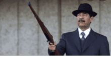 a man in a suit and hat is holding a gun in his right hand .