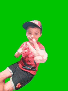 a young boy wearing a hat and a red shirt is making a peace sign .