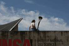 a man sits on top of a wall in front of a sign that says institut national des sciences