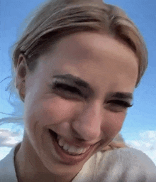 a close up of a woman 's face smiling with a blue sky behind her