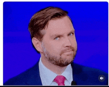 a man with a beard is wearing a suit and tie while standing in front of a microphone .