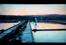 a man is standing on a bridge over a body of water with a sunset in the background and the letters cb on the bottom