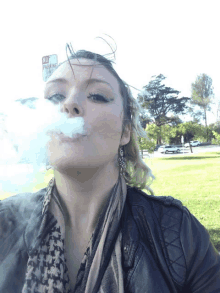 a woman blowing smoke in front of a no parking sign