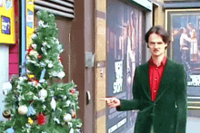 a man in a green jacket points at a christmas tree in front of a building that has the word story on it