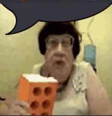 a woman with glasses is holding an orange brick with a speech bubble behind her .