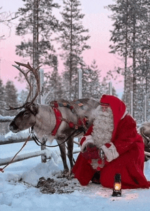 a man dressed as santa claus kneeling next to a reindeer in the snow