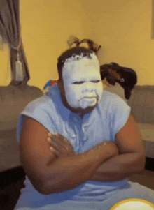 a man with a mask on his face is sitting on a couch with his arms crossed