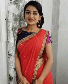 a woman in a red saree and a blue blouse is smiling .