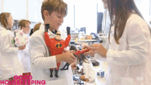 a boy in a lab coat holds a toy in front of a sign that says " good housekeeping "