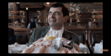 a man in a suit is sitting at a table with a huge pile of food in front of him