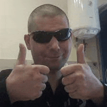 a man wearing sunglasses is giving two thumbs up in front of a heater .