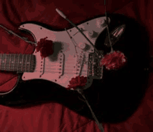 a black electric guitar with red flowers on it is laying on a red blanket .