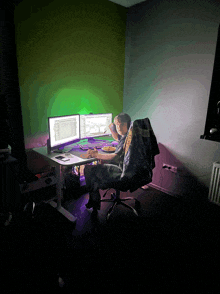 a man sits at a desk with two monitors and a plate of food in front of him