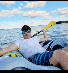 a man laying on a raft holding a kayak paddle and a can of beer in his pocket