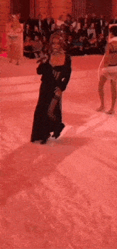 a woman in a black dress is dancing on a red carpet in front of a crowd of people .