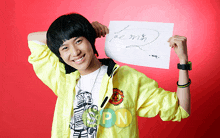 a young man in a yellow jacket is holding up a sign that says tae min