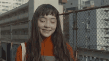 a woman with long hair and bangs is smiling with her eyes closed in front of a chain link fence .