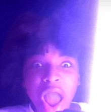 a close up of a person 's face with their mouth open and a purple light behind them .