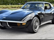 a black corvette is parked on the side of the road in front of a lush green field .