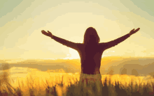 a woman standing in a field with her arms outstretched at sunset