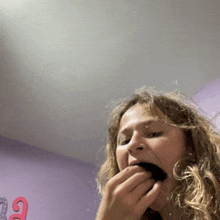 a girl eating a cookie in front of a purple wall with the number 12