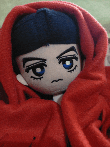 a stuffed doll wrapped in a red blanket with a sad face