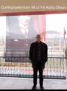 a man stands in front of a banner that says cumhuriyetimizin 98.ci