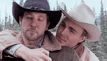 two men wearing cowboy hats are hugging each other in the woods .