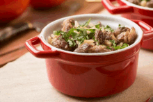 a red pot filled with meat and rice is on a table