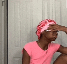 a woman wearing a pink shirt and a pink hat is sitting in front of a white door .