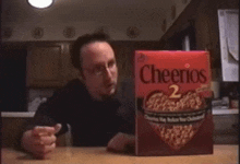 a man is sitting at a table with a box of cheerios