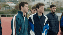 a group of young men are standing on a track and one of them is wearing a blue and white jacket