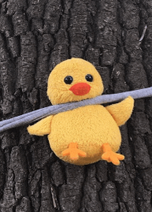 a stuffed yellow chick sitting on a tree trunk