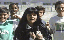 a girl is holding a microphone in front of a group of children who are wearing shirts with the word city on them