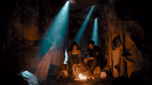 a man and a woman sit in a cave with a fire