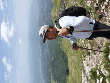 a man wearing a hat with the letter t on it is hiking up a mountain