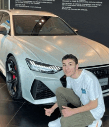 a young man is kneeling in front of a white audi car